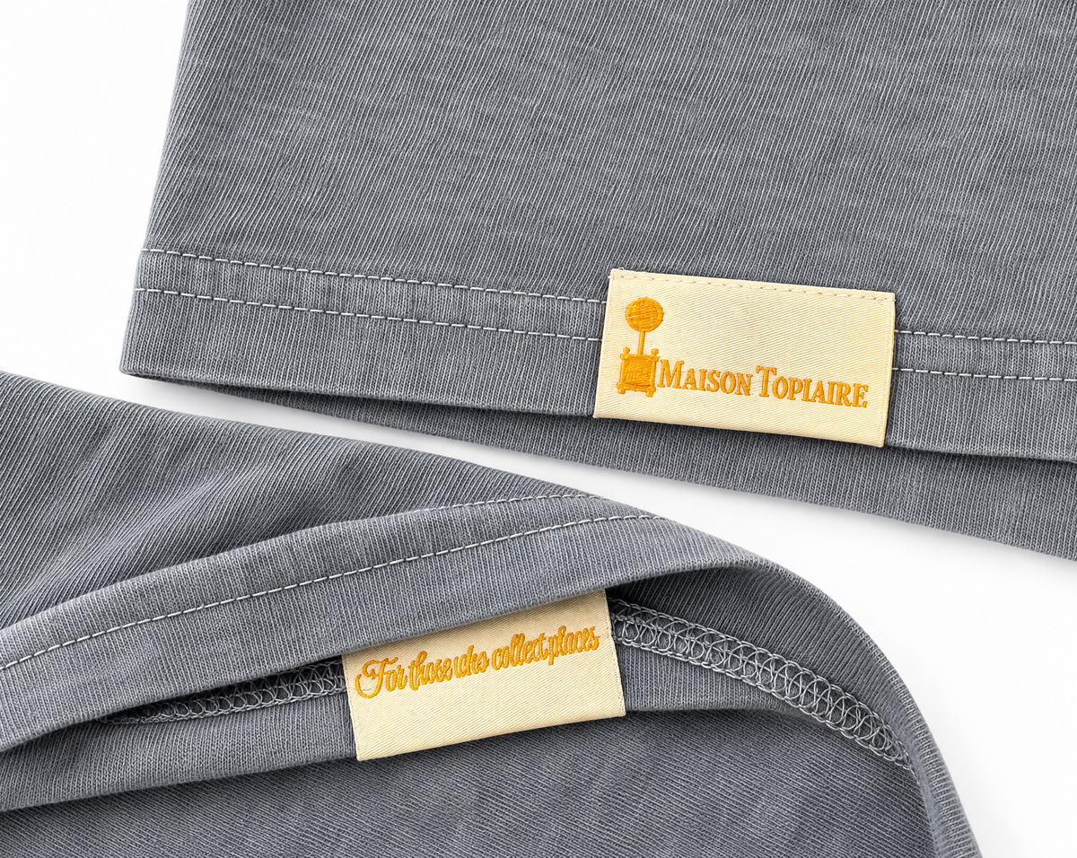 Cream Maison Topiaire labels with golden lettering on grey shirt hems.
