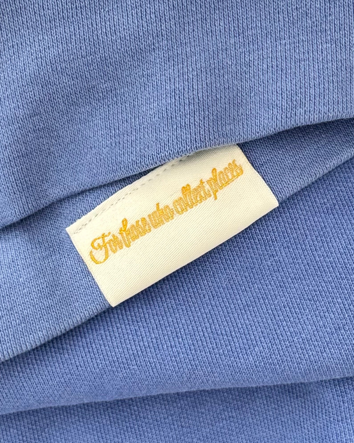 Inward side of the Maison Topiaire woven label shown on a shirt, reading ‘For those who collect places’